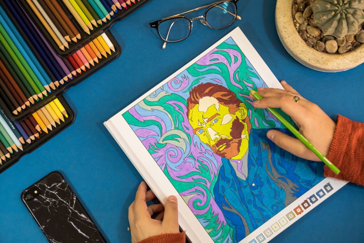 about-us Hands coloring a Van Gogh artwork with vibrant pencils on a blue workspace.