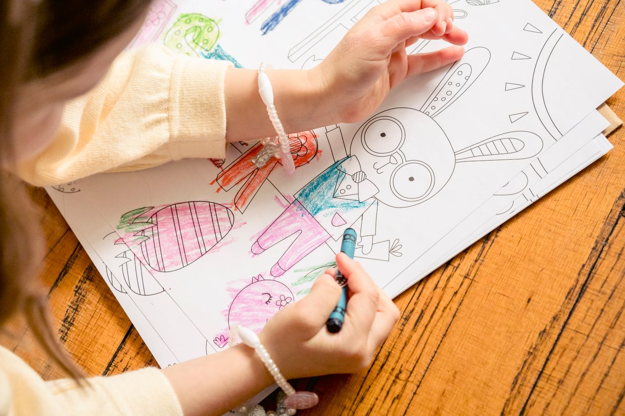 heros-img From above of crop unrecognizable girl in casual clothes drawing in coloring book in daylight